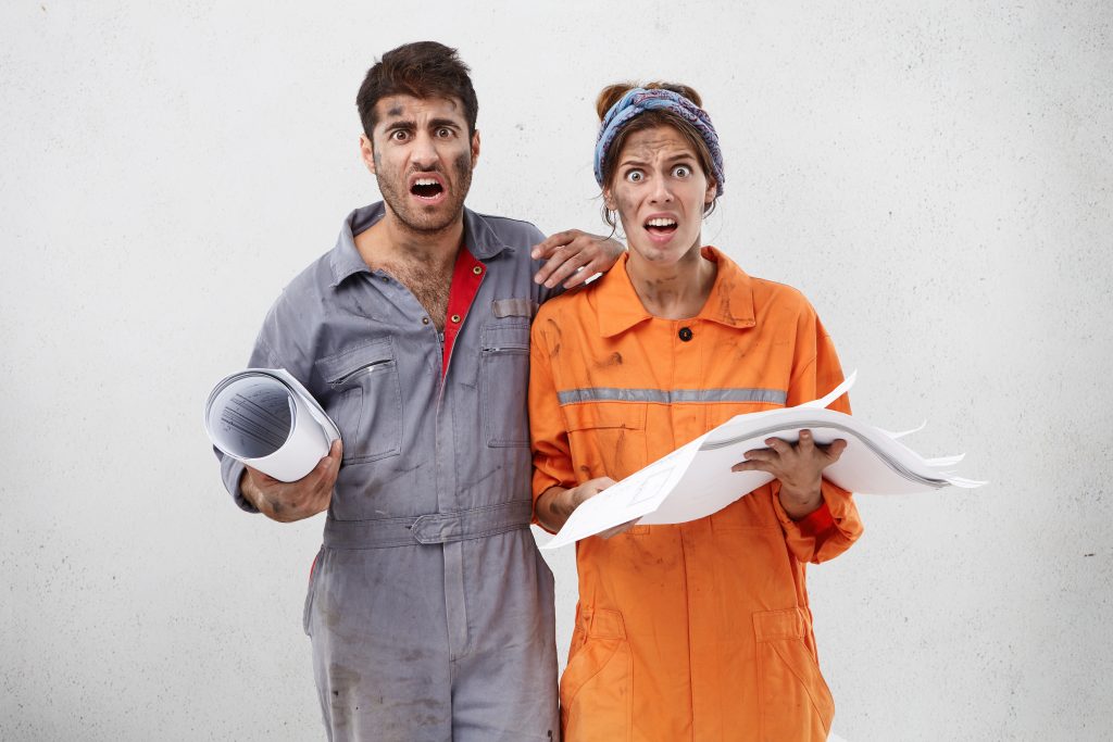 Portait of astonished nervous female and male maintenance workers or carpenters look with unhappy expression, hold blueprint in hands, isolated over white background. Occupation and teamwork concept